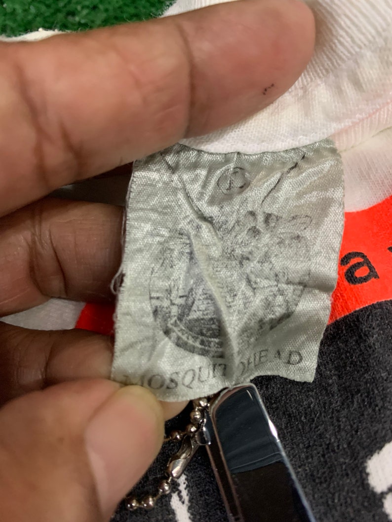 May include: Close-up of a white t-shirt with a black and white graphic print. The tag is visible and reads "Mosquit Head".