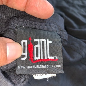 May include: Black tag with white text that reads "giant" with a red stick figure logo. The text "www.giantmerchandising.com" is below the logo. The tag has a white label with the word "medium" on it.