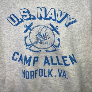 May include: A gray sweatshirt with a blue graphic of the U.S. Navy logo, a Seabee mascot, and the text "U.S. NAVY CAMP ALLEN NORFOLK, VA."