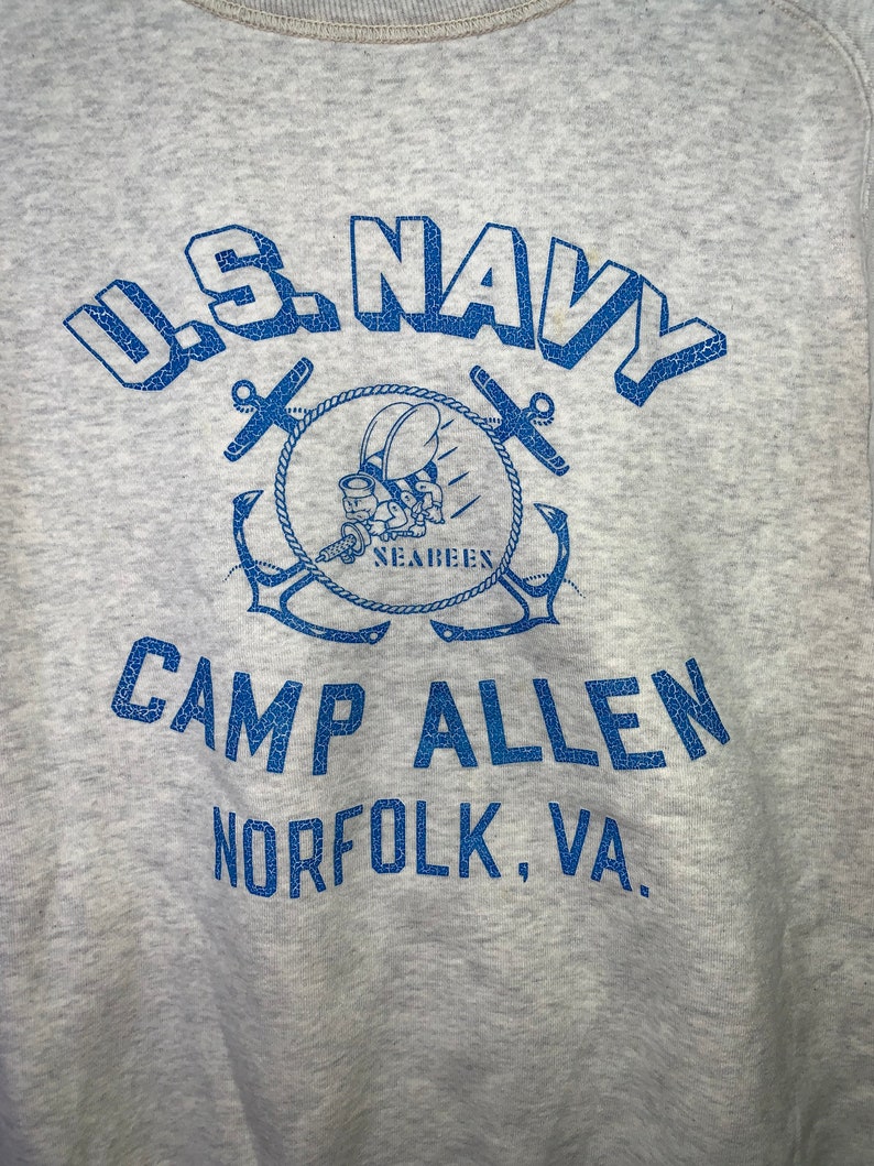 May include: A gray sweatshirt with a blue graphic of the U.S. Navy logo, a Seabee mascot, and the text "U.S. NAVY CAMP ALLEN NORFOLK, VA."