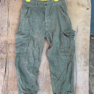 Può includere: Un paio di pantaloni cargo verdi con più tasche e una patta con bottone.