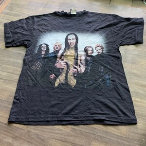May include: Black t-shirt with a graphic print of a band. The band members are wearing black clothing and have long hair. The band's name is "Marilyn Manson".
