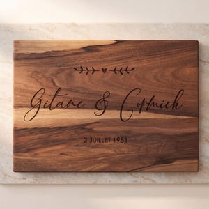 A wooden cutting board with the names "Guitare & Corniche" engraved on it, along with the date "2 JULET 1983".