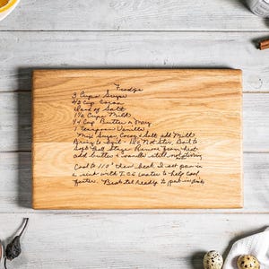 May include: A rectangular light brown wooden cutting board featuring a dark engraved handwritten recipe for fudge. The text includes ingredients like sugar, cocoa, salt, milk, butter, and vanilla, along with detailed cooking instructions for the fudge.