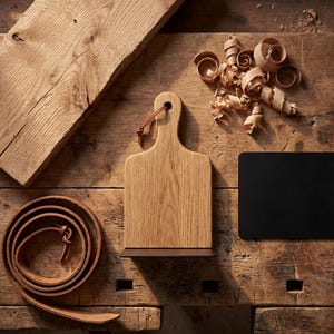 a wooden table with various items on it, including a wooden cutting board, a leather belt, and some wood shavings.