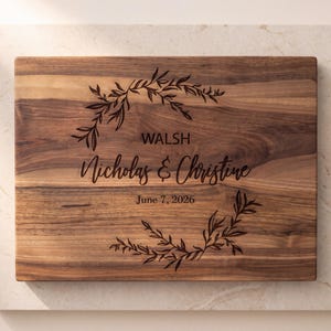 A wooden cutting board with a decorative wreath design and text that reads "WALSH Nicholas & Christine June 7, 2026".