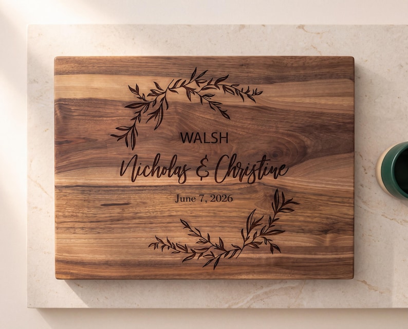 A wooden cutting board with a decorative wreath design and text that reads "WALSH Nicholas & Christine June 7, 2026".