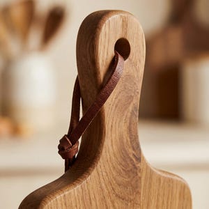 A wooden cutting board with a leather strap attached to it.