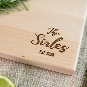 A wooden cutting board with the name "The Sirles" engraved on it, along with the year "EST. 2025" below it.