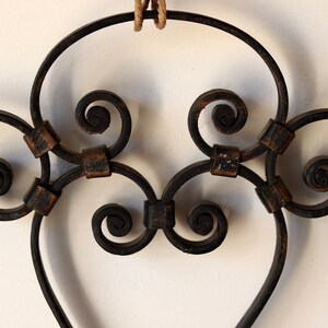 Op de afbeelding: Een zwarte metalen hartvormige wanddecoratie met ingewikkelde krulwerk en een rustieke afwerking.