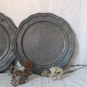 May include: Two antique pewter plates with a scalloped edge. The plates are gray and have a worn, rustic look.