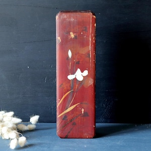 May include: A red wooden box with a white flower design. The box is decorated with a floral pattern and has a slightly distressed look.