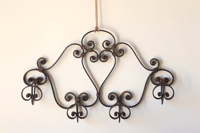 Op de afbeelding: Een zwart metalen wanddecoratief stuk met een gerold ontwerp en vijf haken. Het stuk hangt aan een bruin touwtje.