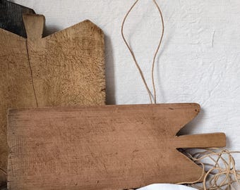 Può includere: Due taglieri di legno, uno con manico, sono esposti su una superficie di lino bianco. I taglieri sono usurati e hanno un aspetto rustico.