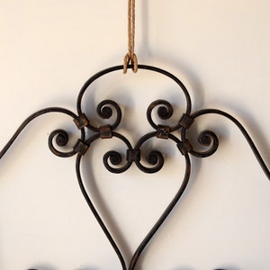 Op de afbeelding: Een zwart metalen hoofdbord met een decoratief scroll-ontwerp. Het hoofdbord hangt aan een touw.