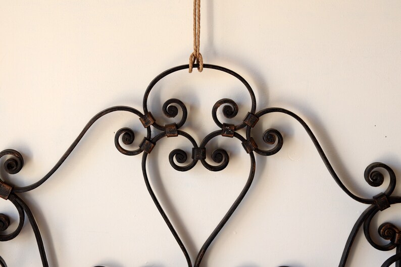 Op de afbeelding: Een zwart metalen hoofdbord met een decoratief scroll-ontwerp. Het hoofdbord hangt aan een touw.