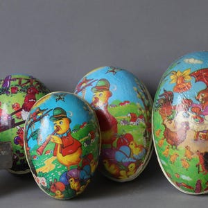 May include: Four vintage Easter eggs made of papier-mâché with colourful illustrations. The eggs feature a variety of scenes, including a duck playing a flute, a bunny with a basket, and a rooster with a hen.