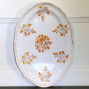 May include: White oval serving platter with a scalloped edge and a floral design in shades of yellow and brown.