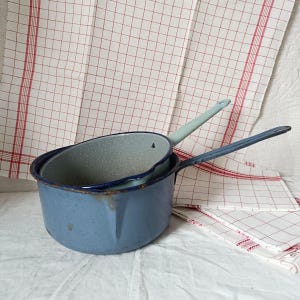 May include: Two blue enamel saucepans with handles, one nested inside the other. The larger saucepan has a speckled blue interior, while the smaller saucepan has a light blue interior.