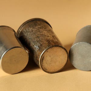 Op de afbeelding: Drie antieke metalen bekers in verschillende maten en afwerkingen. De bekers zijn gemaakt van zilver- en bronskleurige metalen. De beker links is zilverkleurig, de middelste beker heeft een gehamerde textuur en de rechter beker is donkergrijs.