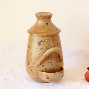 Puede incluir: Un tarro de cerámica marrón moteado con tapa y un pequeño pico lateral. El tarro tiene una asa y un esmalte marrón moteado.
