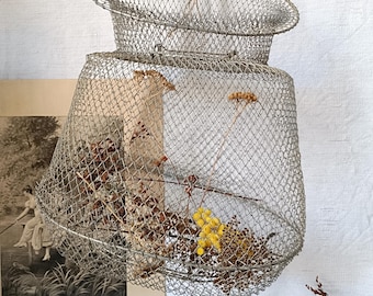 Puede incluir: Un conjunto de dos cestas de malla de alambre, colgadas de un cordón de hilo. Las cestas están hechas de alambre de color plateado y tienen forma de cono. Las cestas están llenas de flores y ramas secas.