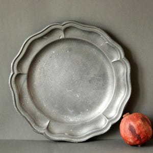 May include: A pewter plate with a scalloped edge. The plate is gray and has a worn, antique look.