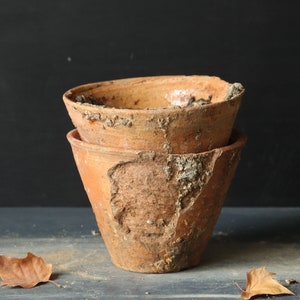 Puede incluir: Dos macetas de terracota, una apilada sobre la otra. Ambas macetas están desgastadas y tienen un aspecto rústico.