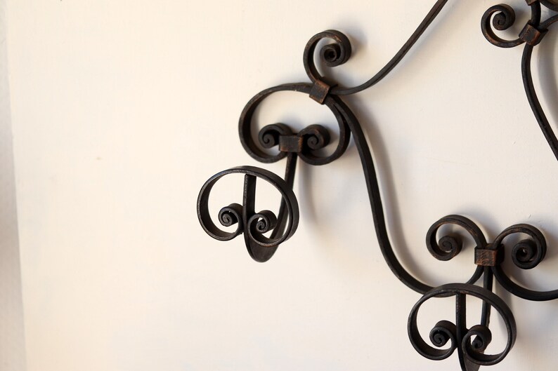 Op de afbeelding: Een zwarte metalen wandbevestigde kapstok met sierlijke kruldetails. De kapstok heeft drie haken.