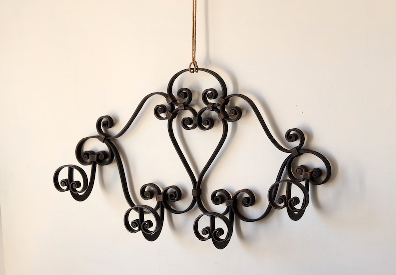 Op de afbeelding: Een zwarte, gesmede wandhaak van ijzer met een decoratief scroll-ontwerp en zes haken.
