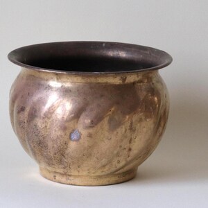 May include: A brass planter with a wavy, textured design. The planter is a light gold color and has a round shape.