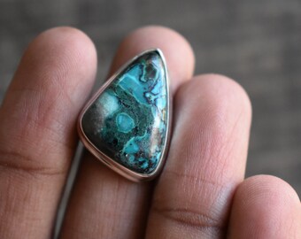 Könnte beinhalten: Ein dreieckiger Silberring mit einem blauen und grünen Edelstein. Der Edelstein hat ein wirbelndes Muster aus Blau, Grün und Schwarz.