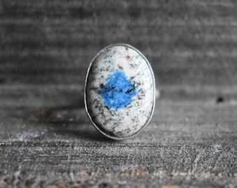 May include: A silver ring with a blue and white oval stone. The stone has a blue center with white speckles.