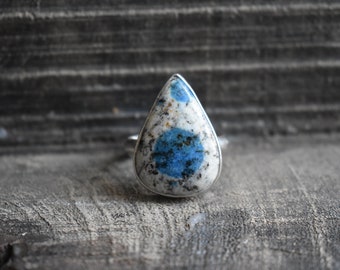 May include: A teardrop-shaped ring with a blue and white stone set in silver.