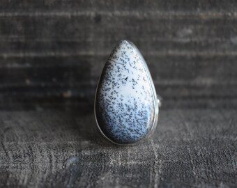 May include: A teardrop-shaped ring with a white and black dendritic opal stone set in silver.