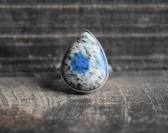 May include: A teardrop-shaped ring with a blue and white stone set in silver.