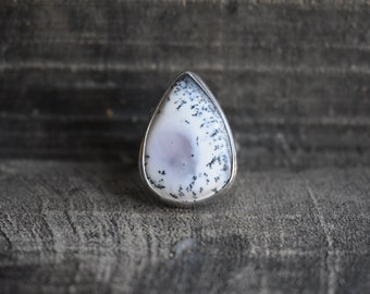May include: A teardrop-shaped ring featuring a white and black dendritic agate stone set in sterling silver.