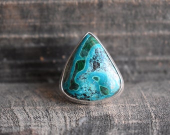 Könnte beinhalten: Ein tropfenförmiger Ring mit einem blauen und grünen Edelstein, der in Silber gefasst ist.