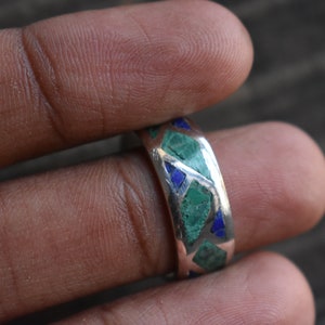 May include: A silver ring with green and blue stones set in a geometric pattern.