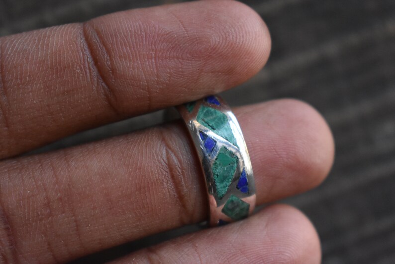 May include: A silver ring with green and blue stones set in a geometric pattern.