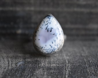 May include: A teardrop-shaped ring featuring a white and black dendritic agate stone.