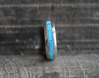 May include: A silver ring with a turquoise inlay. The turquoise is set in a thin band of silver and is a light blue color.