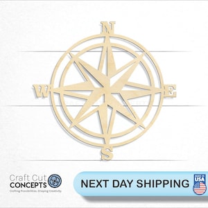 May include: A wooden compass rose cut-out with directional markers for North, South, East, and West. The compass is made of light-colored wood and is set against a white background. The text "Craft Cut Concepts" is visible at the bottom left.
