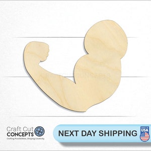 May include: A wooden cutout of a bicep flexing, in a light brown color. The cutout is made of unfinished wood and is ready to be painted or stained.