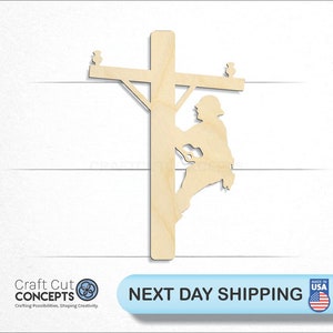 May include: Wooden cutout of a lineman climbing a utility pole. The lineman is wearing a hard hat and safety gear. The pole has two crossbars with insulators.