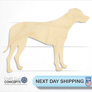 May include: A wooden cutout of a dog in a standing position. The dog is facing to the right. The cutout is made of light brown wood.