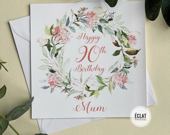 May include: A white card with a watercolor floral wreath in shades of green and pink. The text "Happy 90th Birthday Mum" is written in a cursive font in coral pink.