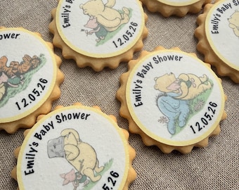 Puede incluir: Varias galletas redondas con borde festoneado amarillo. Cada galleta tiene una parte superior circular blanca con una ilustración de personaje de Winnie the Pooh y el texto "Emily's Baby Shower 12.05.26" en negro. Están dispuestas sobre una superficie texturizada de color neutro.