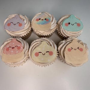 May include: Six cupcakes with beige frosting, each topped with a flat, circular edible decoration featuring a different pastel-colored dumpling character with a smiling face, rosy cheeks, and various patterns including sparkles and rainbow gradients.