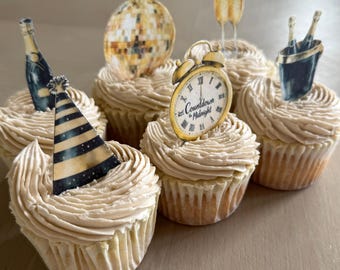 May include: A collection of cupcakes with tan frosting, each decorated with New Year's Eve themed toppers. Toppers include a party hat, disco ball, champagne bottle, champagne glasses, a clock with the text "Countdown to Midnight", and a champagne bucket.